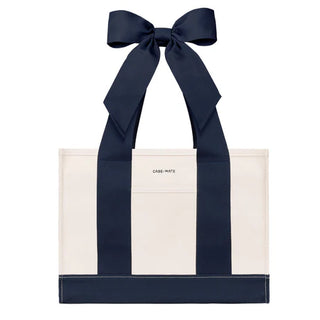 An off-white canvas tote bag with bold navy blue vertical stripes and matching navy ribbon handles tied in a large bow. The brand name 'CASE-MATE' is printed in small black letters on the front pocket.