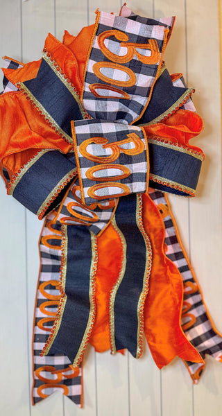 Hand-tied Halloween bow featuring black-and-white gingham “BOO” ribbon, vibrant orange ribbon, and black ribbon with gold and orange beaded trim.
