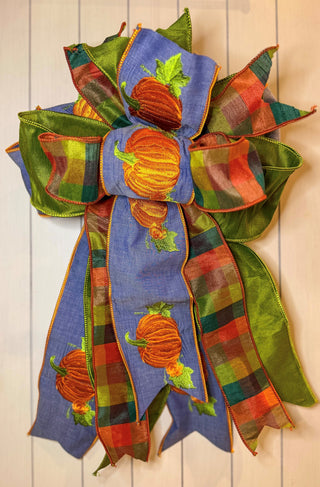 Hand-tied fall bow featuring blue ribbon embroidered with orange pumpkins, multicolor plaid ribbon, and rich green ribbon.