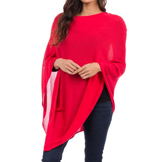 A woman wearing a red bamboo knit poncho with a 3/4 length sleeve, posing with one hand against her chest.