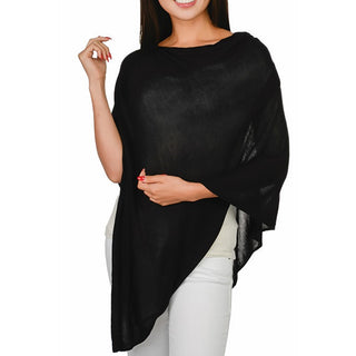A woman smiling, wearing a black bamboo knit poncho with a 3/4 length sleeve, over a white top and white pants.