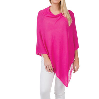 A woman wearing a pink bamboo poncho over a white top, paired with white pants.