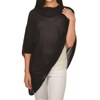 A navy bamboo poncho, one size, displayed on a model who is facing to the side and has her hand adjusting the poncho. The model is wearing white pants.